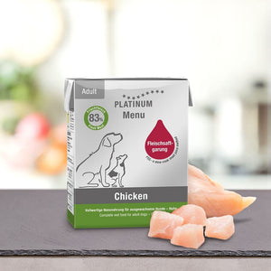 Škatla PLATINUM Paket različnih okusov Mokre Hrane za Pse za odrasle pse stoji na pultu poleg kosov sveže mesa, na embalaži pa so ilustracije psov in informacije o izdelku v nemščini in angleščini, ki poudarjajo visoko prebavljivost.